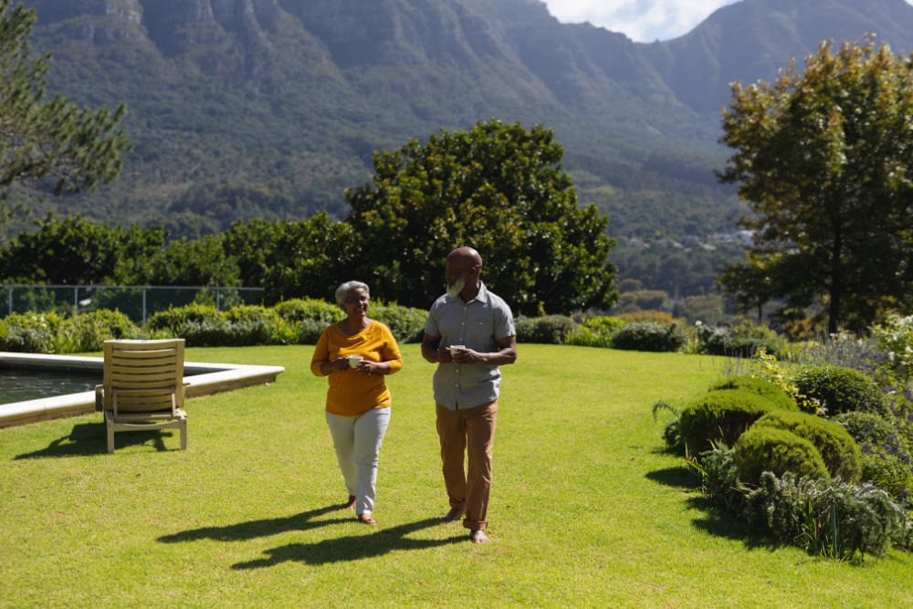 A senior couple walking together in a garden with mountains in the background.