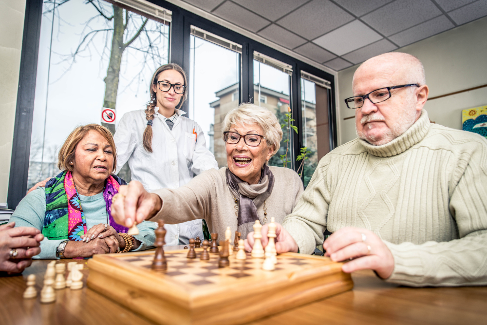 Seniors playing chess with a caregiver in a cozy indoor setting.