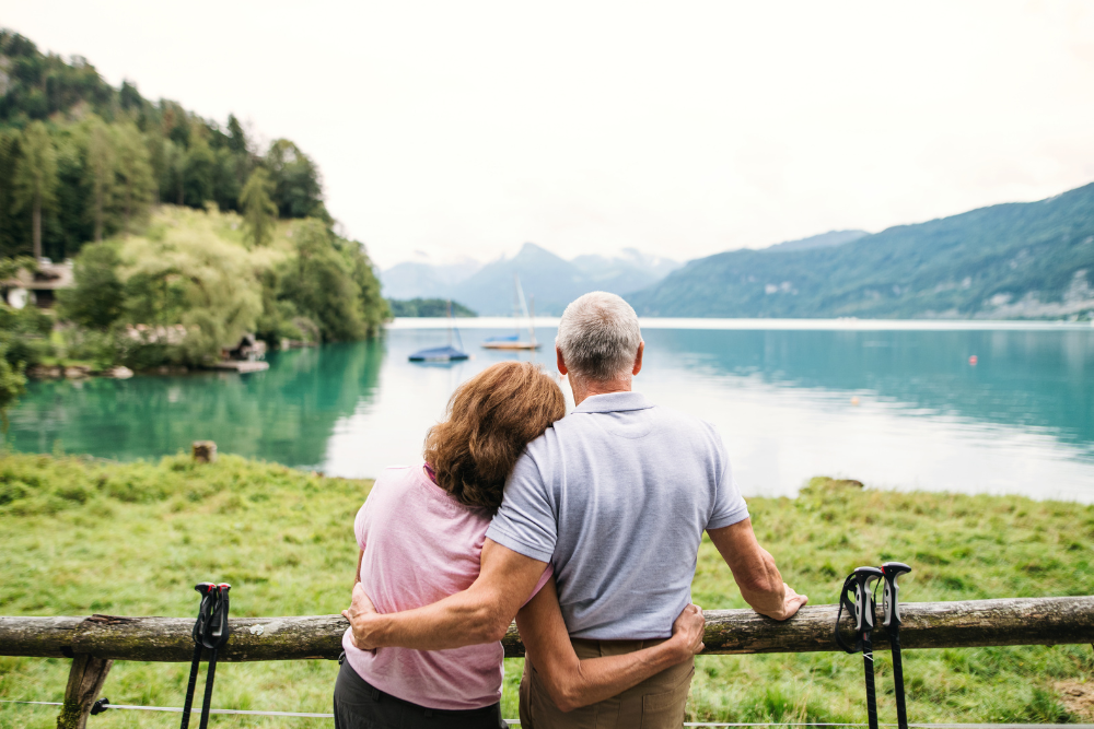 A senior couple standing by a lake with mountains in the background.