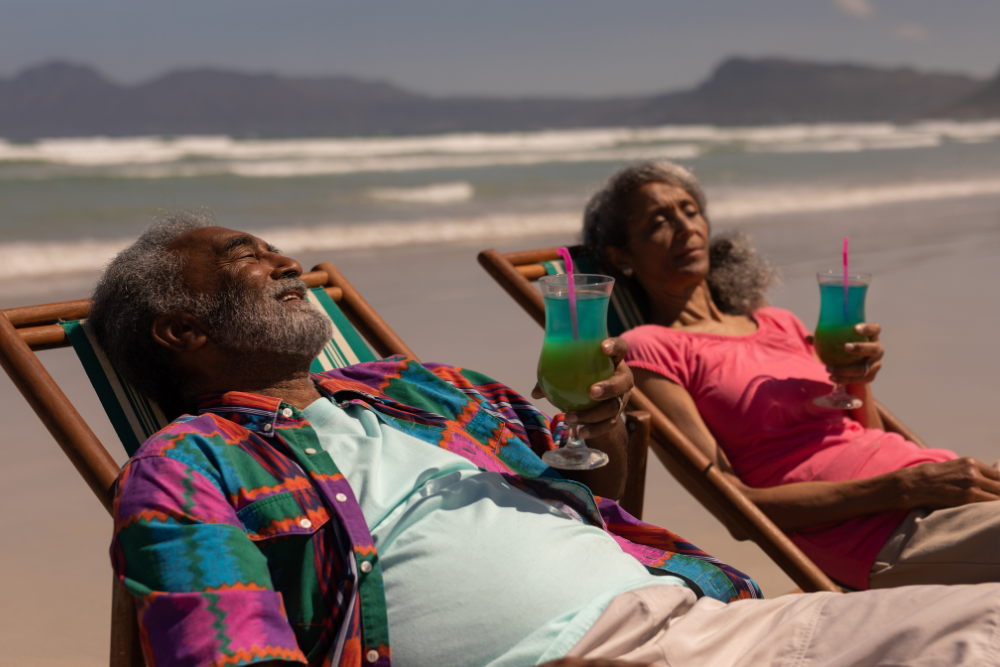 Senior couple lounging on beach chairs by the sea, sipping colorful drinks and enjoying the sun.