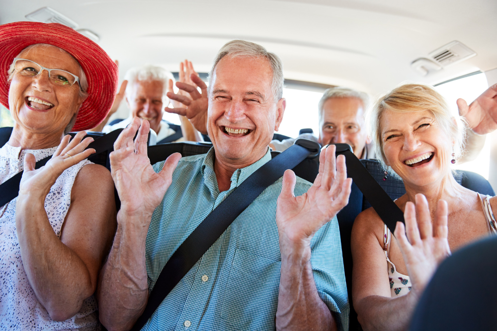 Group of seniors smiling and waving hands while sitting in a car during a road trip.