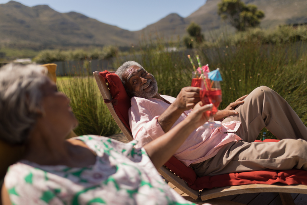 Elderly couple lounging on beach chairs by the sea, sipping colorful drinks and enjoying the sun.