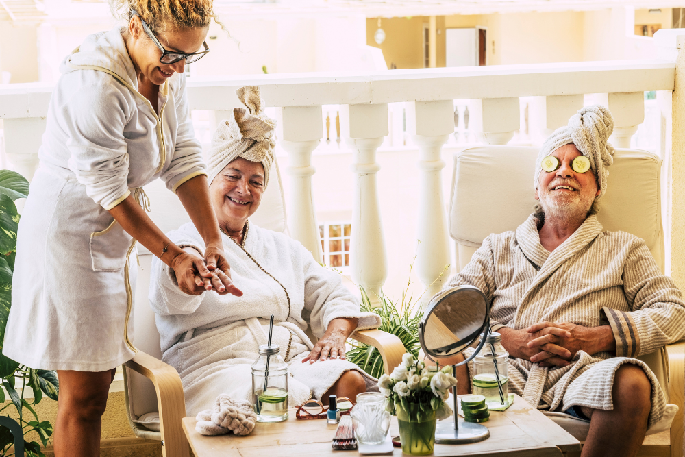 Senior couple enjoying a spa day with hand treatments and cucumbers on their eyes, smiling contentedly.