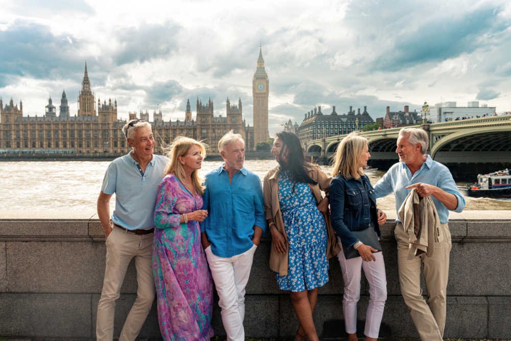 Group of older friends enjoying a day out by the River Thames with the Houses of Parliament and Big Ben in the background.