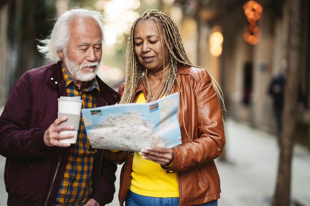 Senior couple reading a map together on a street, with one holding a coffee cup.