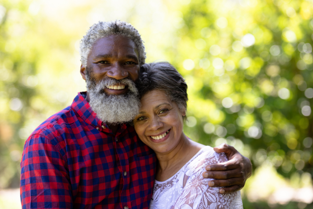 Happy older couple embracing each other and smiling in a sunny outdoor setting.