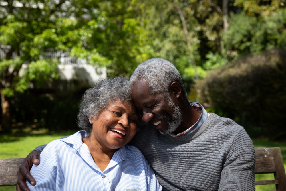 Smiling elderly couple sitting on a bench and enjoying a moment together in a lush green garden.