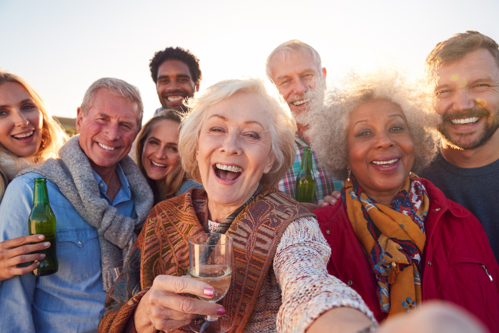 Group of diverse senior friends taking a selfie while enjoying drinks together outdoors