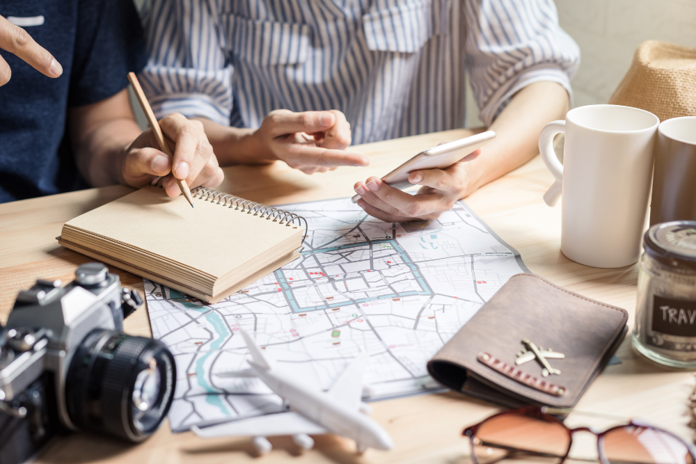 Two people planning a trip with a map, notebook, and smartphone on a table.