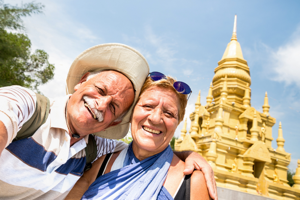 Senior couple taking a selfie in front of a golden temple on a sunny day.