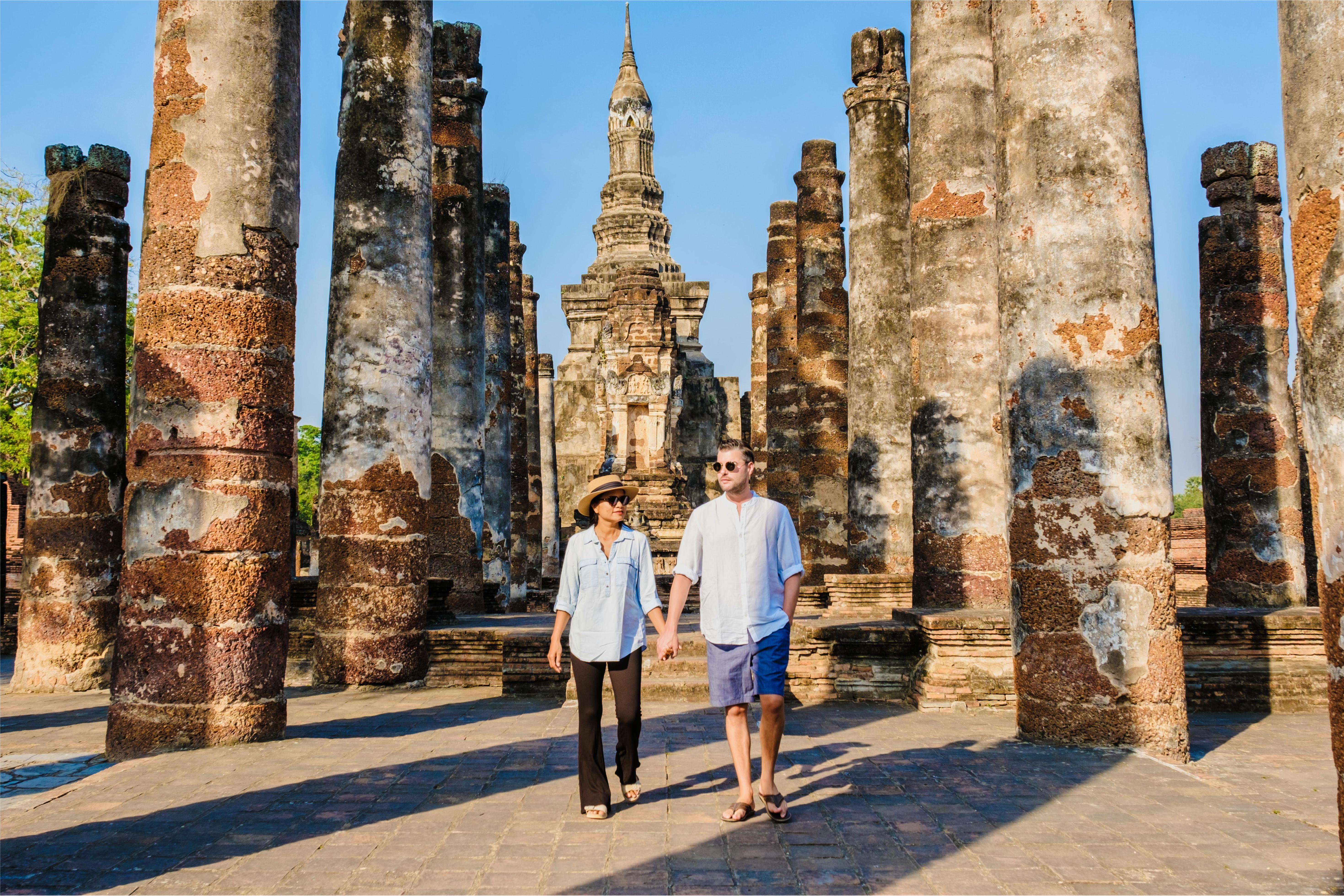 Couple visiting Wat Mahathat in Sukhothai Old City, Thailand, walking among ancient columns.