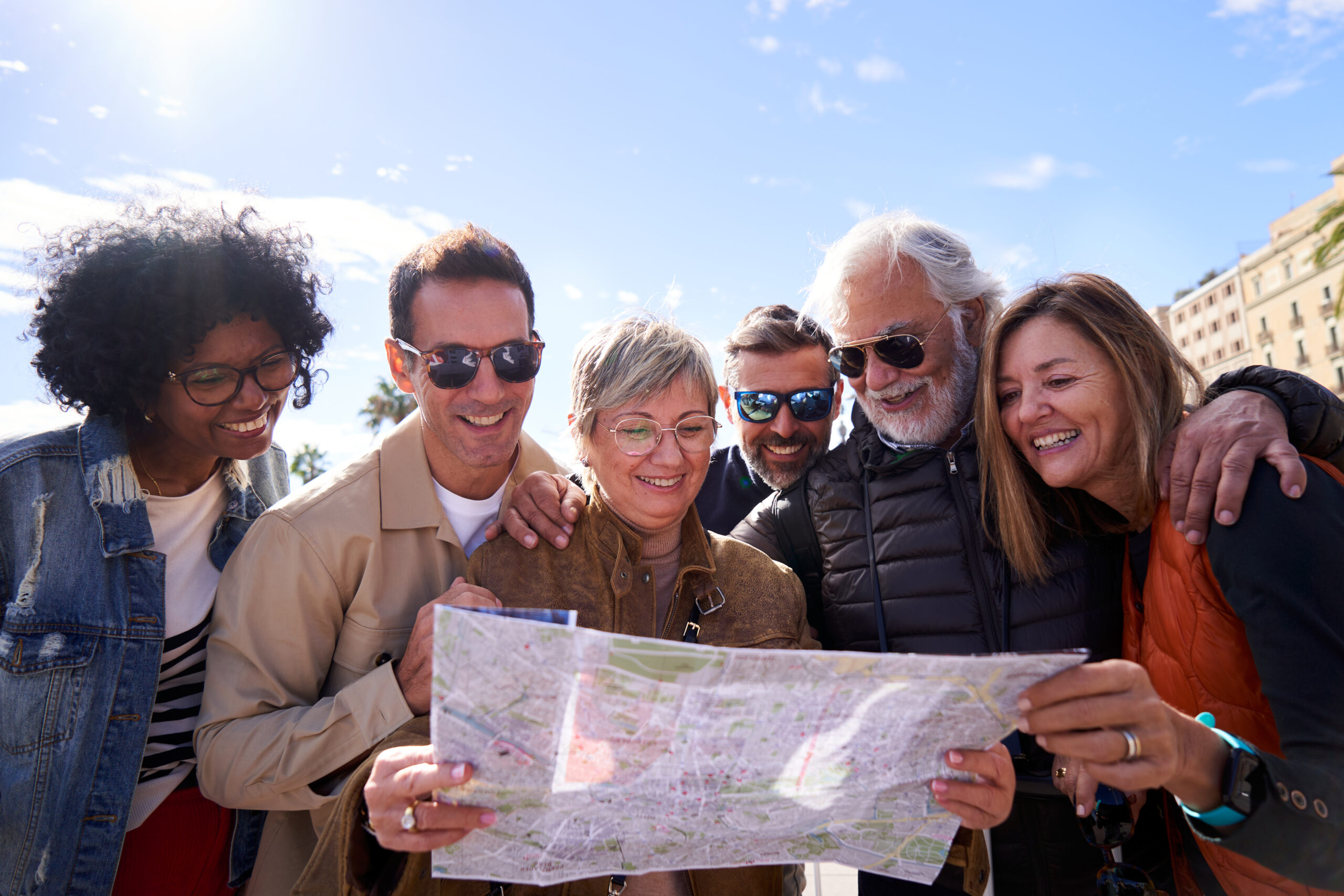 Group of diverse mature friends smiling and looking at a map together outdoors.