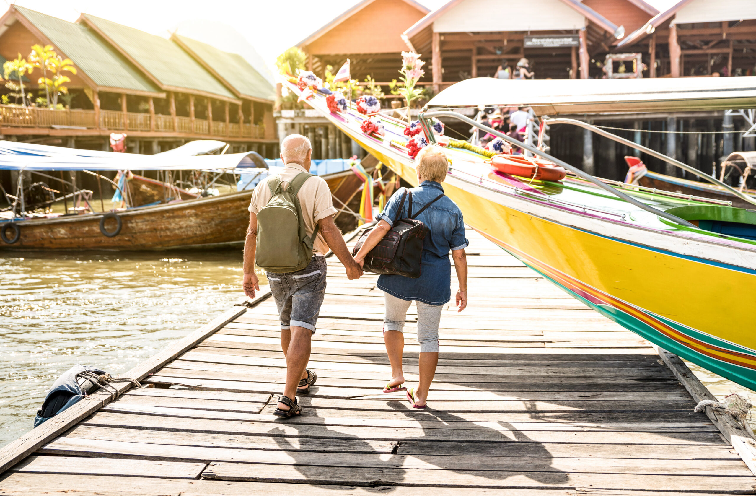 Senior couple holding hands while walking on a dock towards a boat.