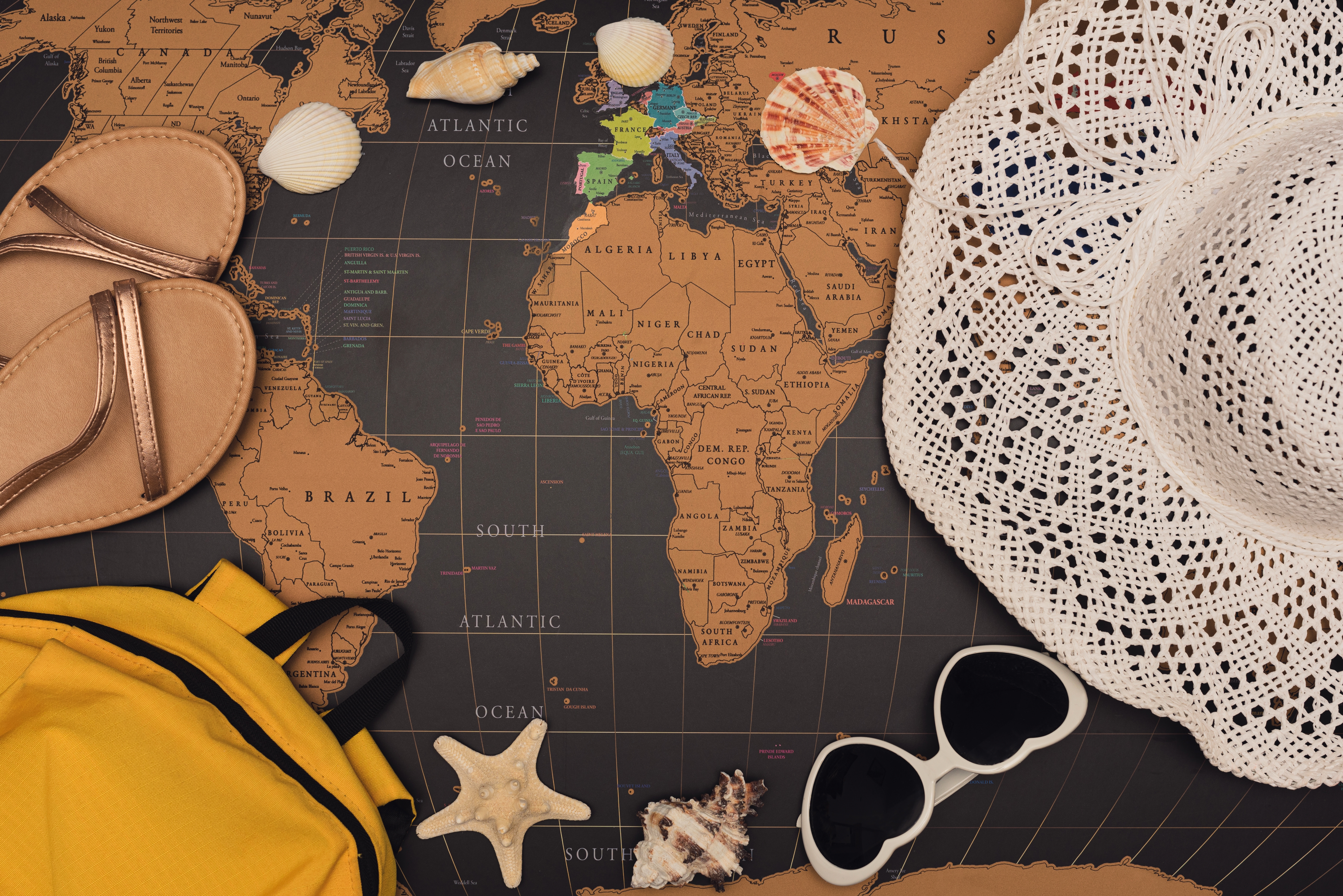 Travel essentials including a hat, sunglasses, backpack, sandals, and seashells arranged on a world map.