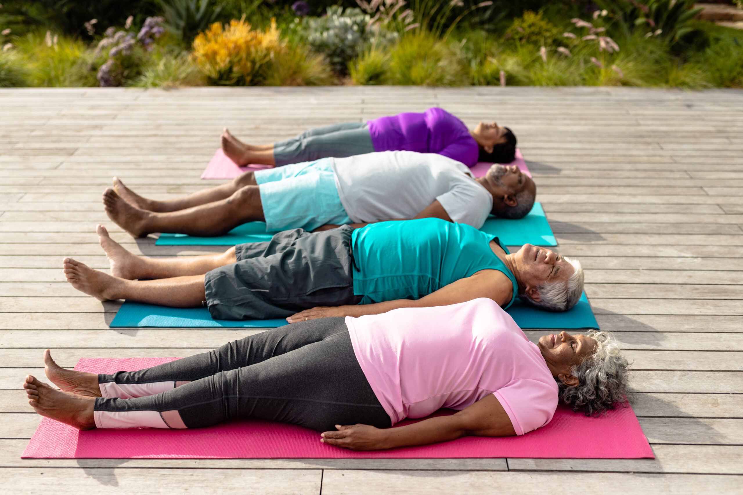 Group of elderly people lying on yoga mats in a relaxing outdoor yoga session