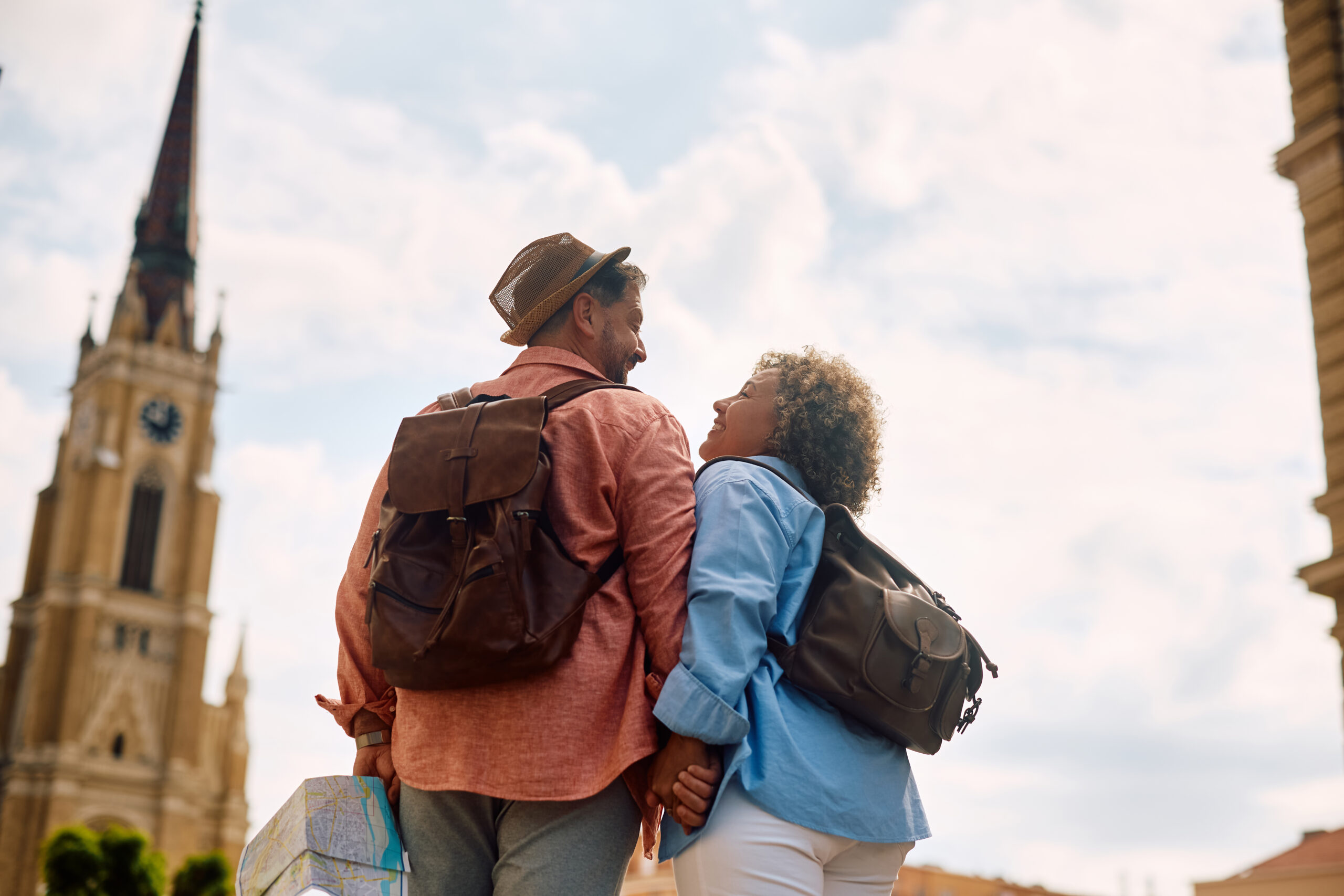 A middle-aged couple with backpacks holding hands and walking through a city street.