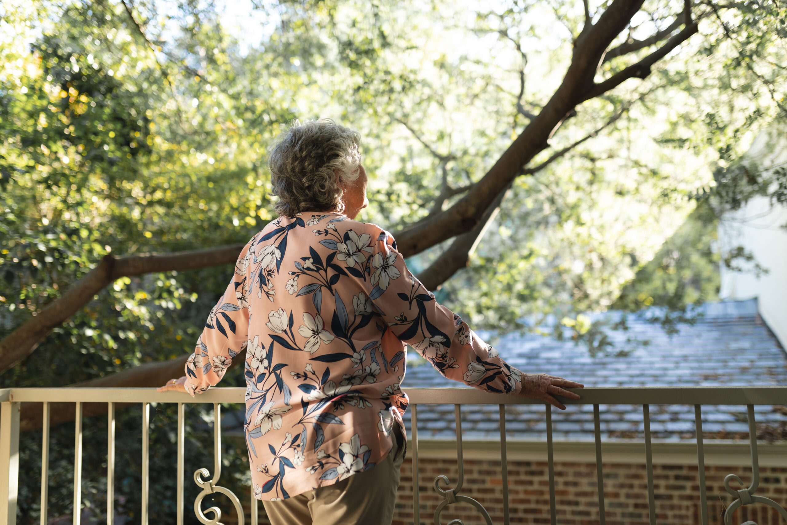 Senior woman standing on a balcony looking out at the trees.