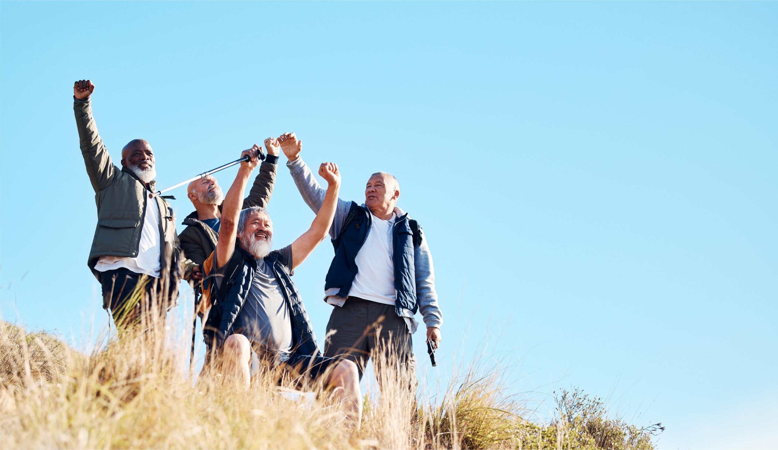 Group of senior men celebrating a successful hike in nature with raised arms.